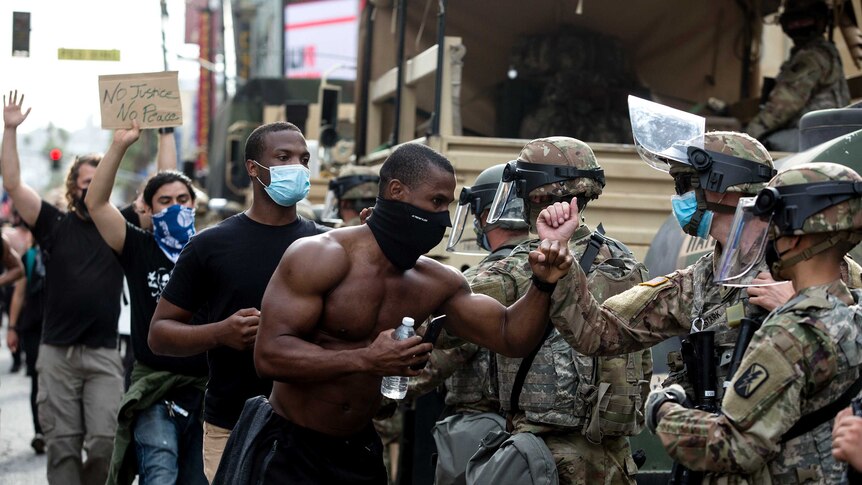 A shirtless man wearing a face masks bumps elbows in a gesture of respect with a uniformed National Guardsman while protesting
