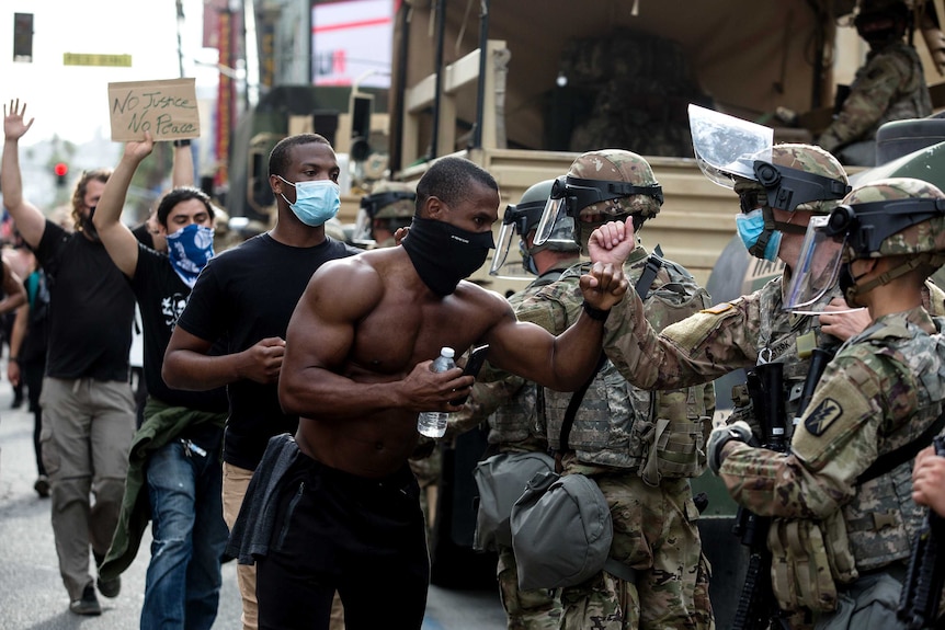 A shirtless man wearing a face masks bumps elbows in a gesture of respect with a uniformed National Guardsman while protesting