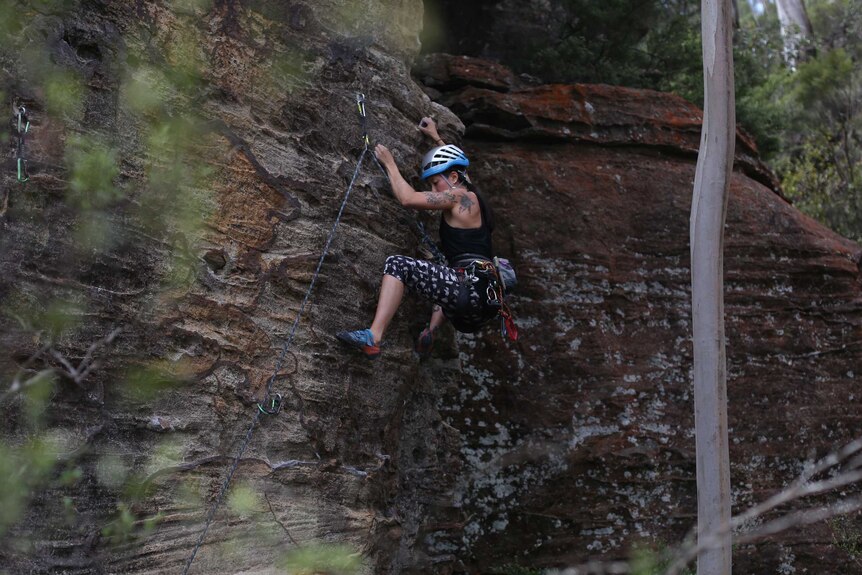 A rock climber looks downwards while hanging from the face of a large rock