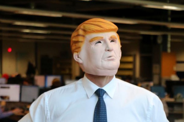 A man poses in a Donald Trump mask.