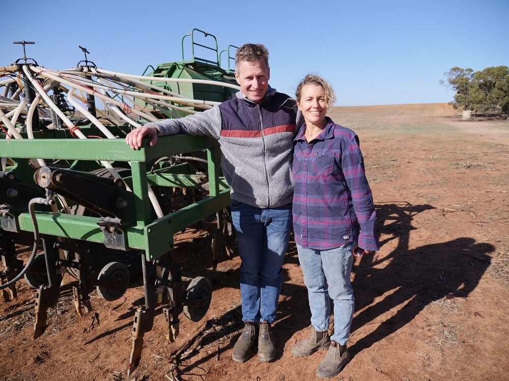 Man and woman stand by a machine that sows seed direct into the soil