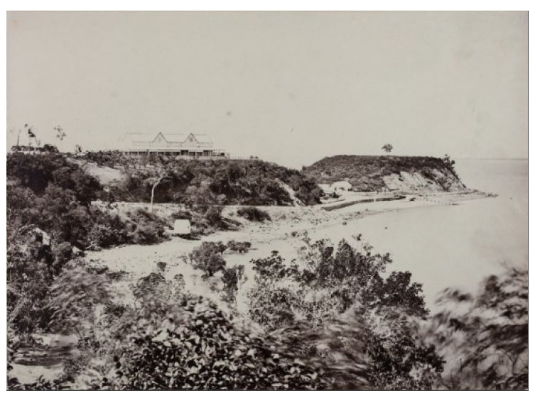 An old photo of a building on top of a cliff near a beach