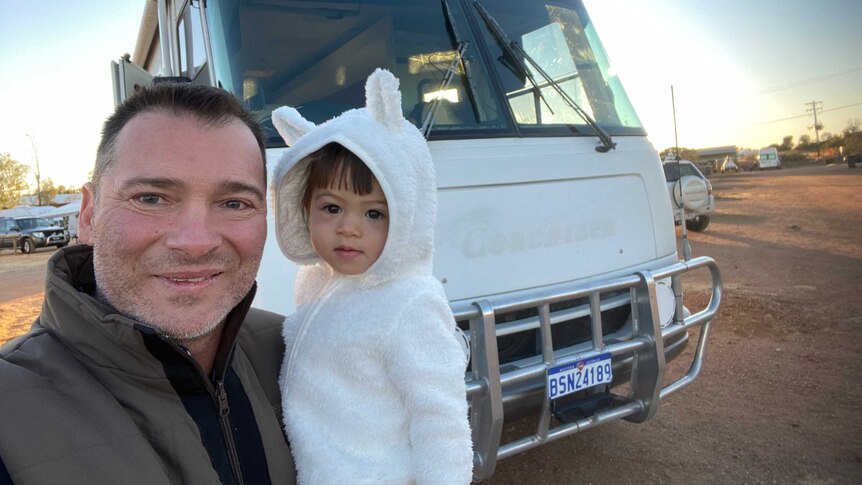 Country singer Adam Brand holding his young daughter in front of motorhome
