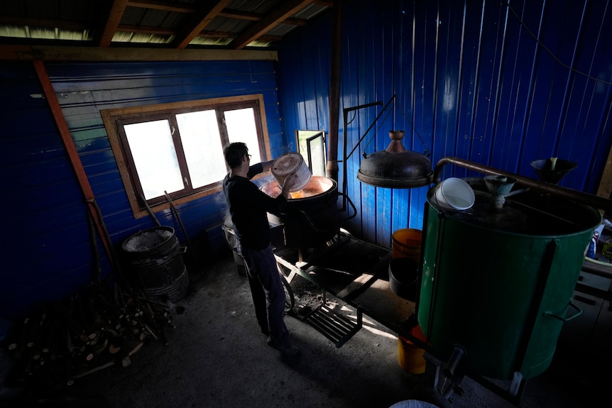 A man empties contents into an oven inside a blue shed