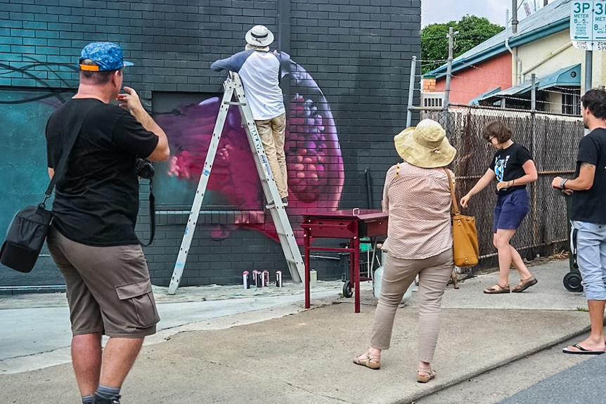 Residents and visitors watch on as Zookeeper works on his art in Highgate Hill.