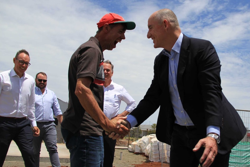 A man in a red cap with a large smile shaking hands with a minister in a suit.