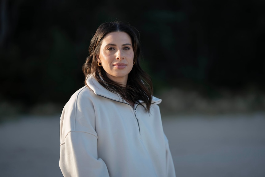 Woman in a white sweatshirt standing on a beach.