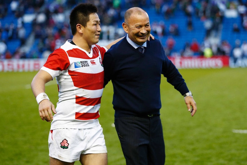 A Japanese male rugby union player with his arm around his coach as they celebrate a Rugby World Cup win in 2015.