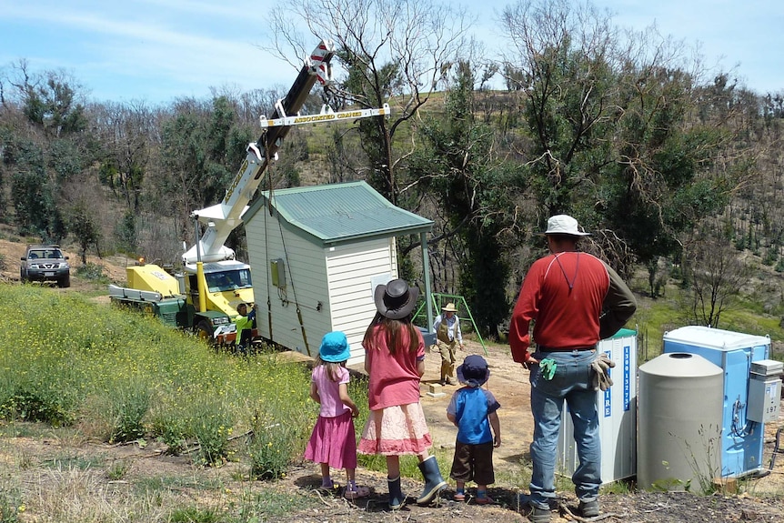 Three young children and a man look out at construction in a field