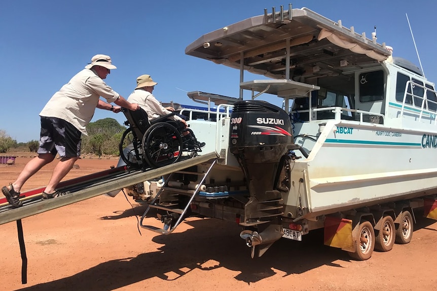 Man pushing father in wheelchair onto finishing boat.