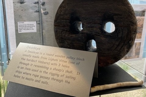 A deadeye pulley block (thin round piece of wood with three holes) on display with card at community hub