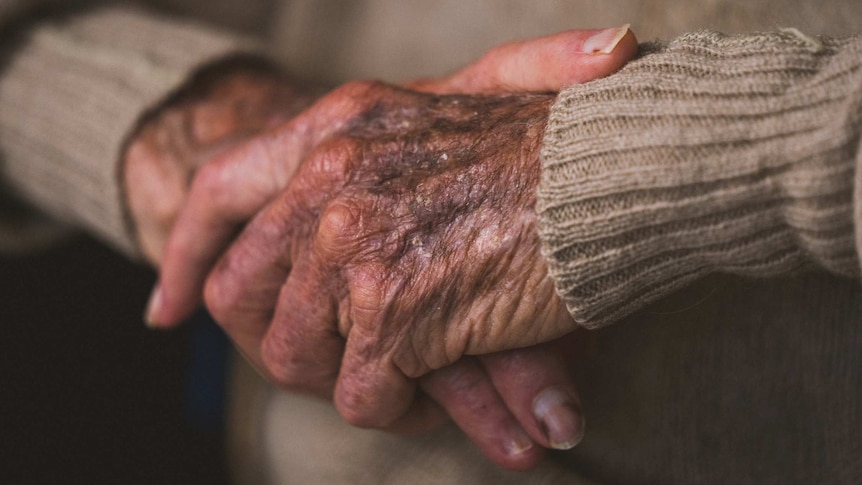 A close-up shot of an old man's hands clasped together.