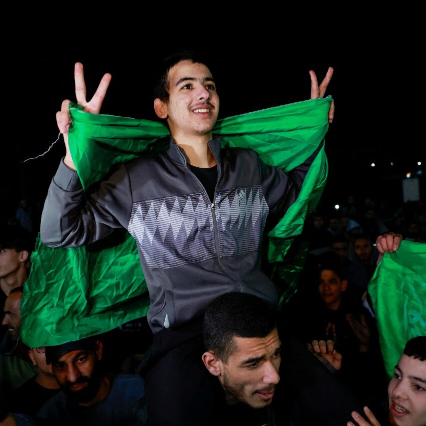 A young boy with a green flag makes the peace sign while sitting on a man's shoulders