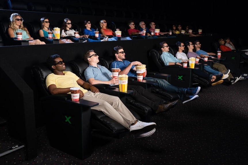 People sitting in reclining cinema seats watching a film.