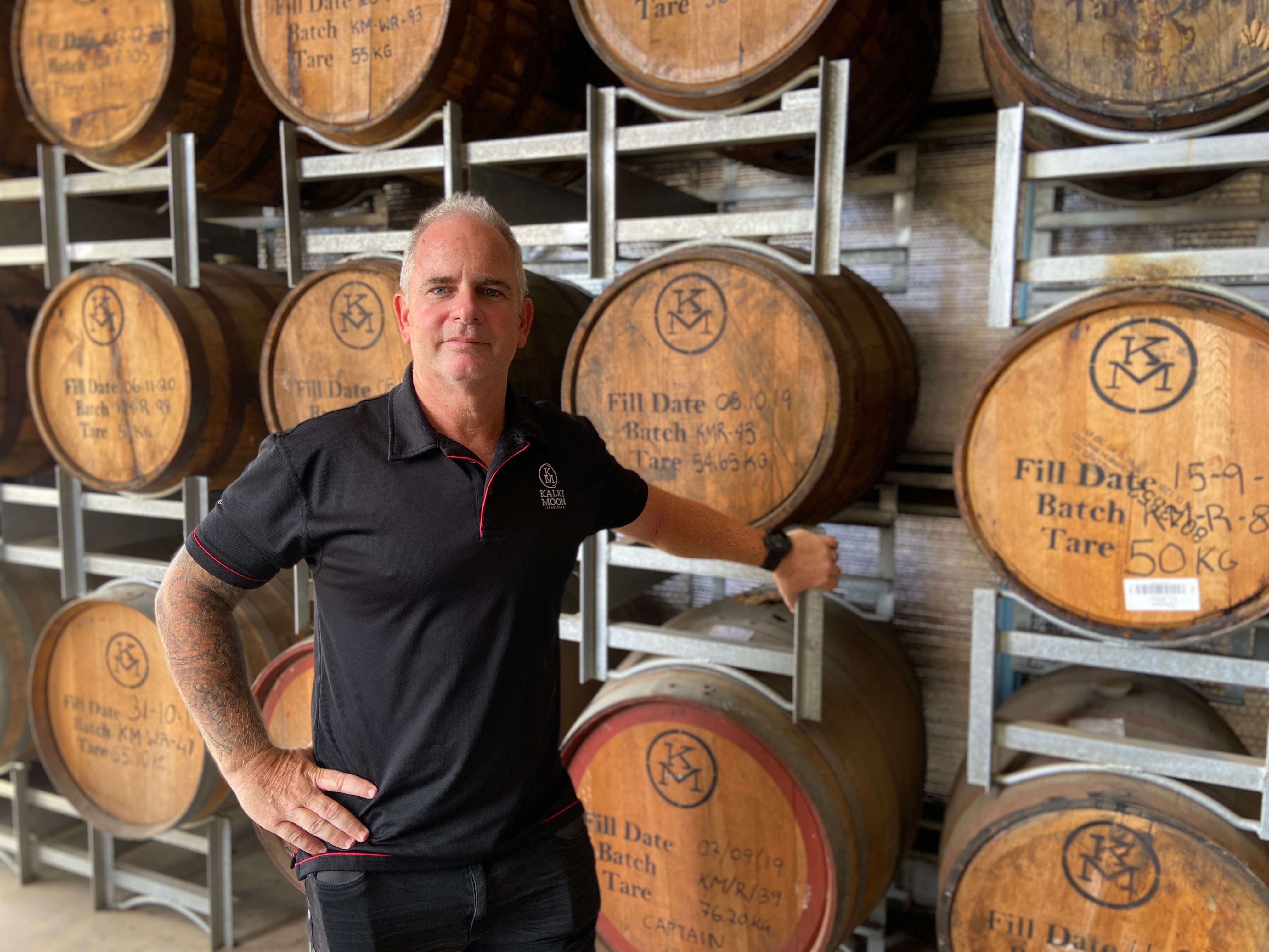 A man leaning against a wall of wooden alcohol barrels.