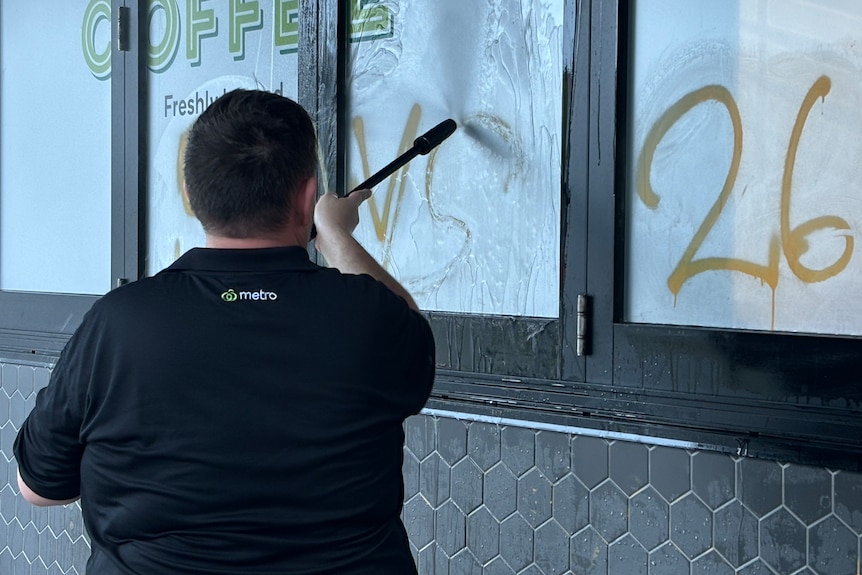 Un employé de Woolworths utilisant un nettoyeur haute pression pour nettoyer les graffitis.