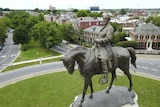 A statue of Robert E Lee on a horse, with red-brick houses and tree-lined streets in the background.