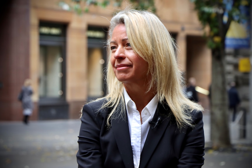 A businesswoman with long blonde hair sits in Sydney's Martin Place looking off to the side of camera.