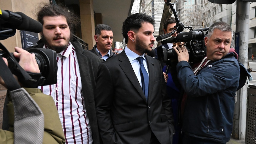 picture of a man wearing suit coming out of a court building and surrounded by journalists 
