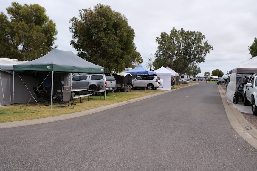 A caravan park road with cars and shelters all down the street. 