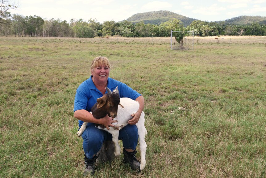 woman kneels holding a goat in a paddock