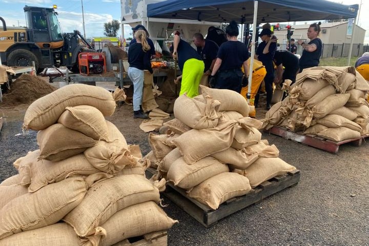 An image of piles of cream coloured sand bags being filled and stacked by people in Moree