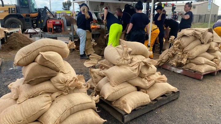 An image of piles of cream coloured sand bags being filled and stacked by people in Moree