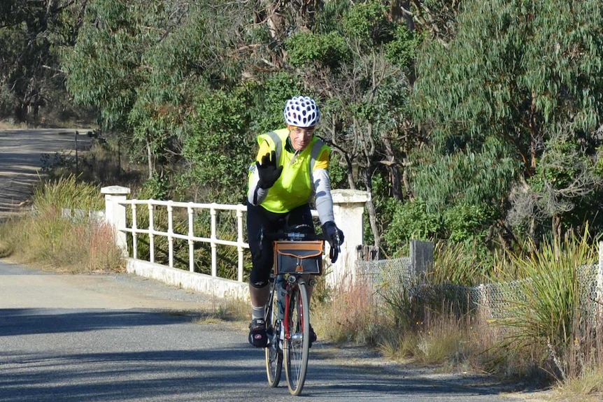 A man wearing fluro and a helmet rides a bicycle