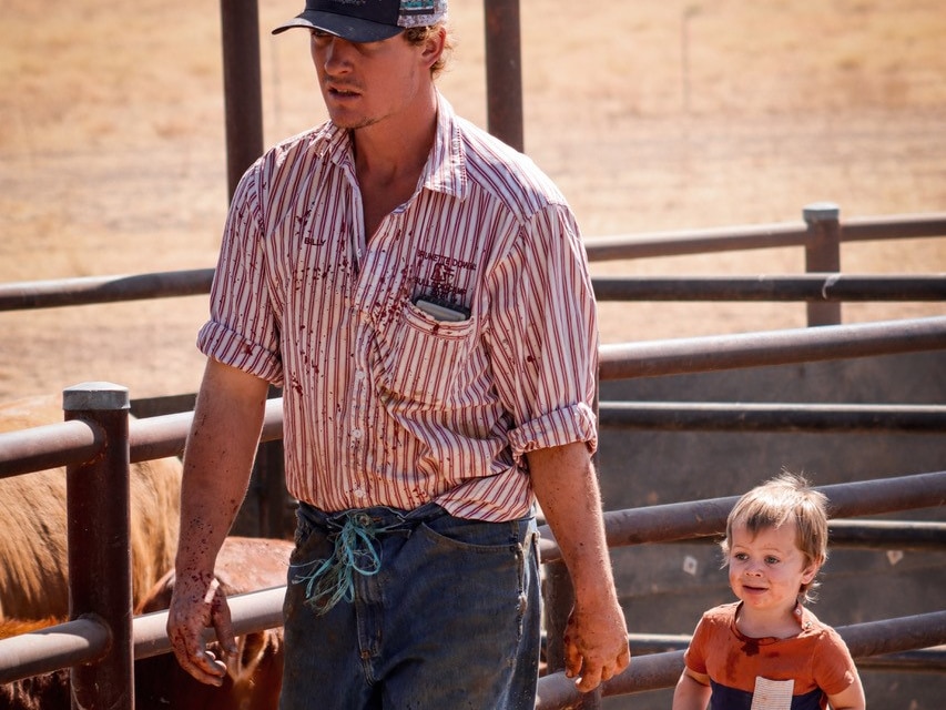Man and toddler walking through a cattle yard. 