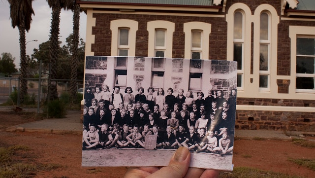 A black and white school class photo is held in front of an old brick building.