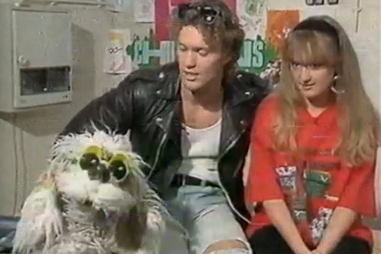 Young man and woman sit close together framed for a TV show with a puppet dog.