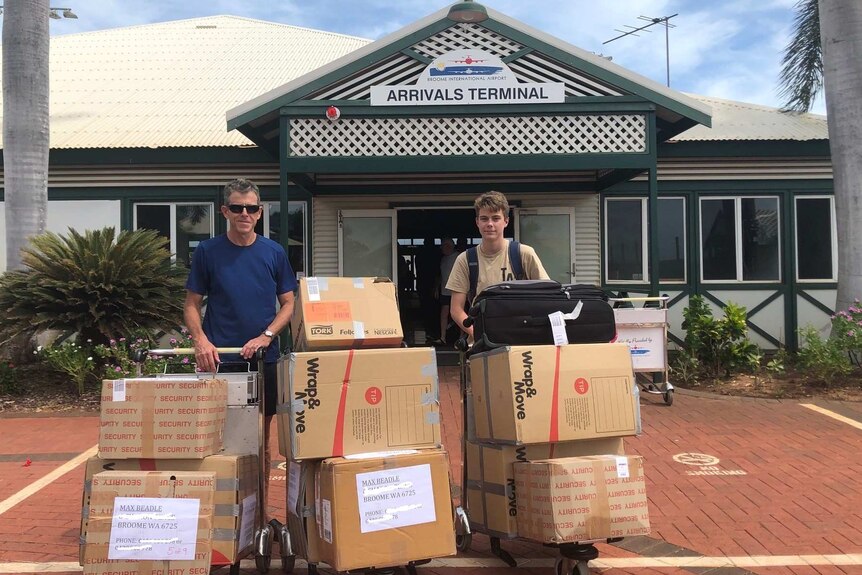 Father and son standing with a number of carboard boxes outside the arrivals terminal at Broome airport
