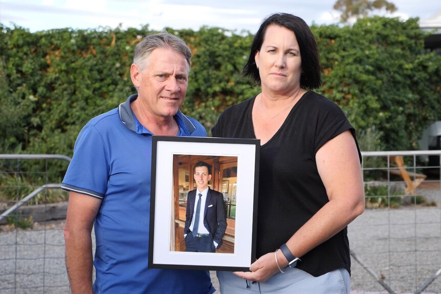 A father and mother hold a picture of their late son.