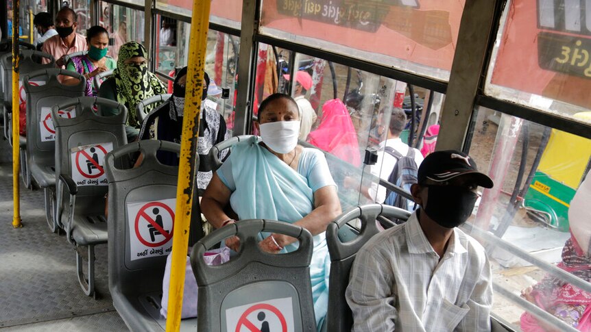 Indian passengers on a bus wear face masks, with signs on every second featuring a "no sitting" symbol.
