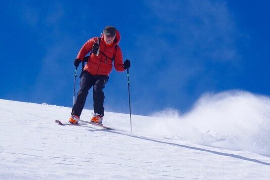 Huw Kingston skis down a hill wearing a red jacket with a blue sky.