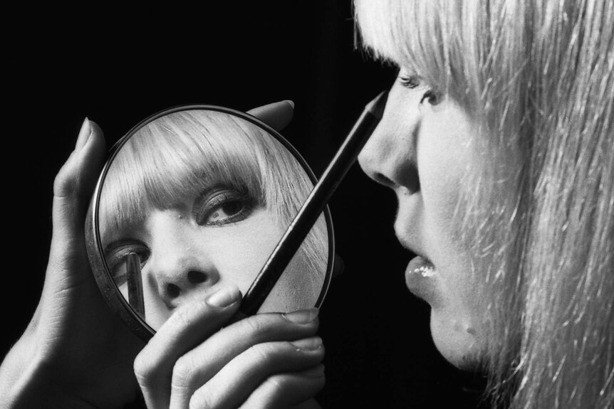 A woman applies eyeliner with a compact mirror.