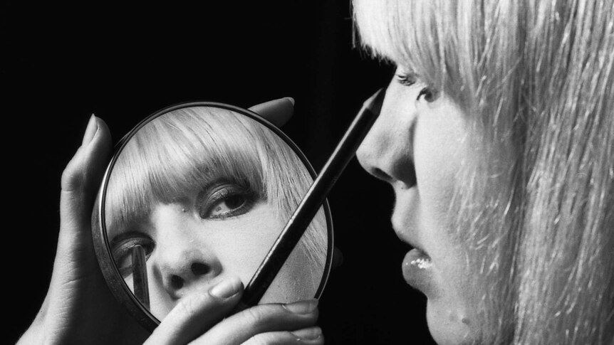 A woman applies eyeliner with a compact mirror.