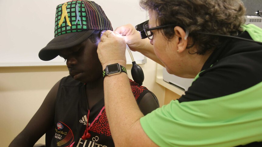 A health worker examining an ear of an Indigenous teenager using a tool.