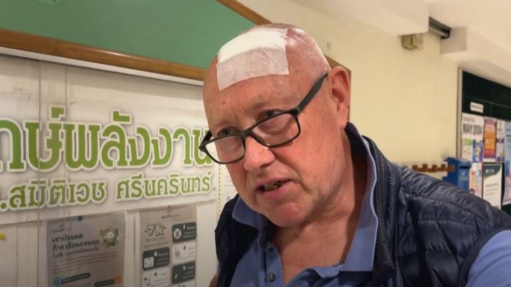 Jerry being interviewed with a bandage on his bald head and glasses. 