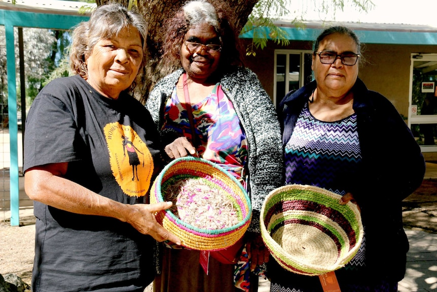Tjanpi desert weavers from NPY lands hold two baskets they have made