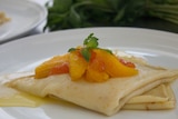 Crepes topped with poached citrus and fresh mint on a white plate.