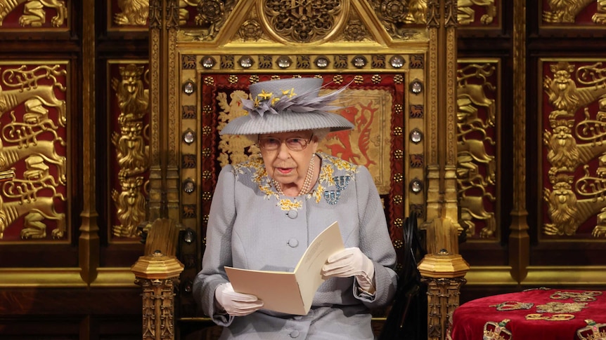 Queen Elizabeth sits on a throne like chair and reads from a speech