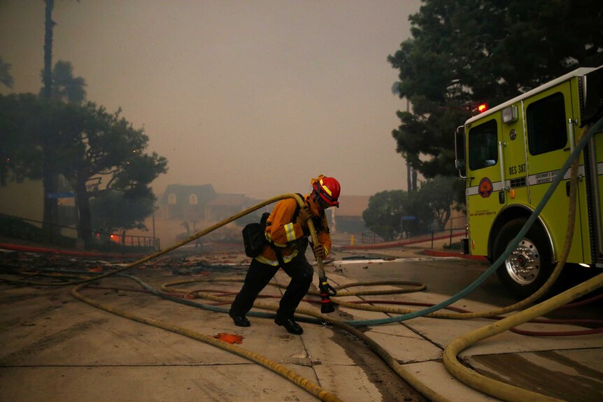 A firefighter carries a hose as a fire burns in Malibu, California