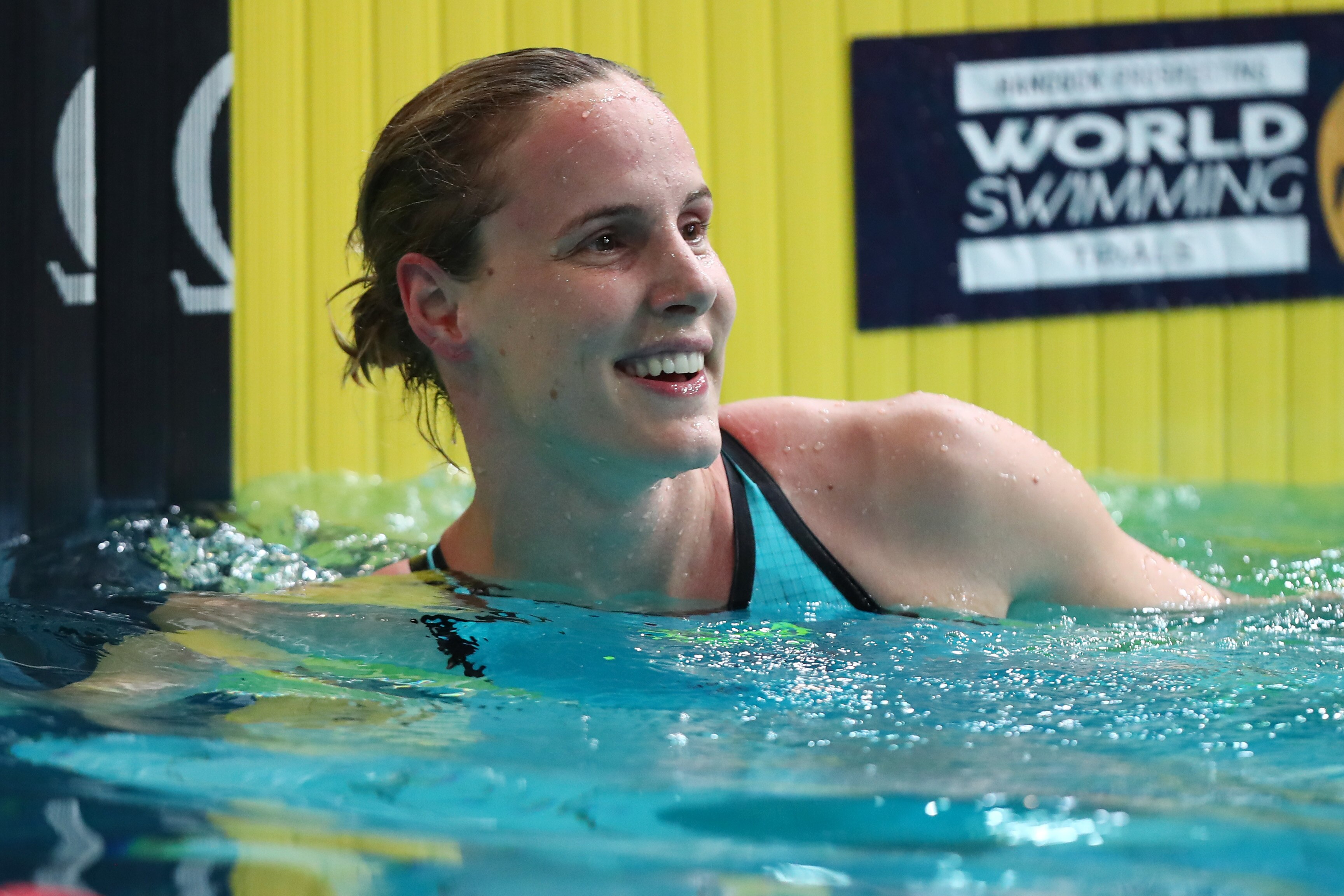 An Australian swimmer with a swim cap on her head looks down the pool after finishing a race.