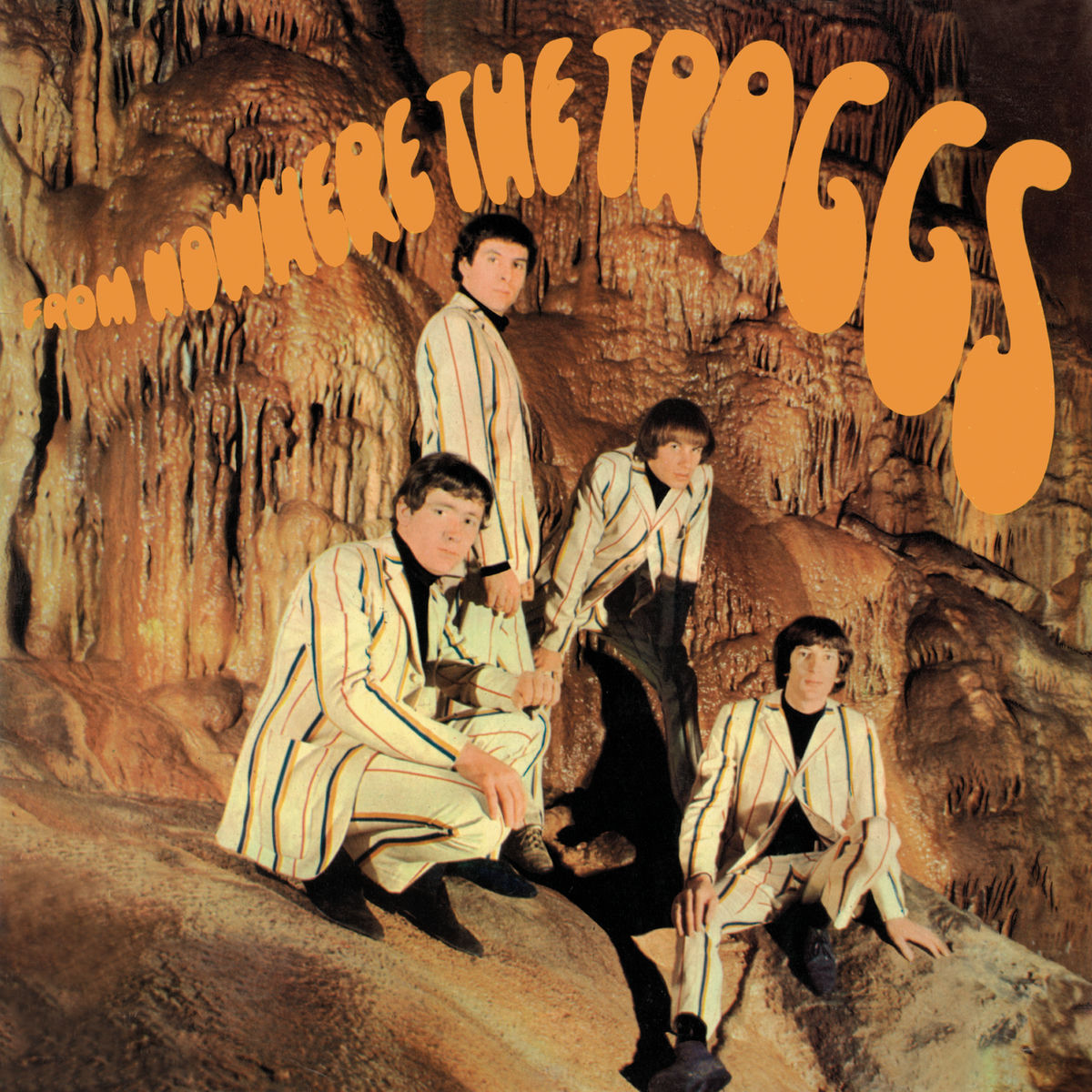 The four band members wear pinstripe suits in a cave