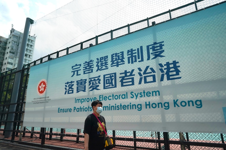 A person walks past a billboard in Hong Kong which writes about the electoral system. 