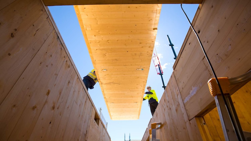 A timber panel is lowered into a construction site.