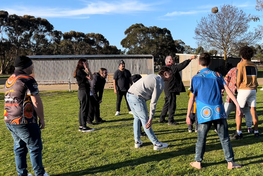 Kids and adults in a paddock throwing around apossum skin ball