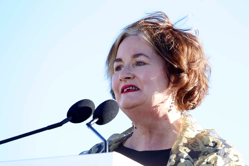 Jackie French speaks at a podium under a clear blue sky.