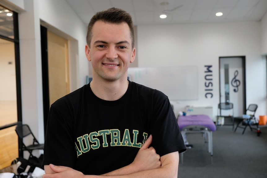 Sam Cartledge smiles with his arms crossed, he wears a t- shirt with Australia written on it.